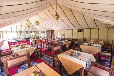a dining room with tables and chairs in a tent at Nomadic Sands Retreat in Merzouga