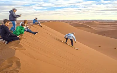 a group of people sitting on a sand dune at ERG MERZOUGA SAHARA CAMP in Merzouga