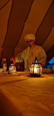 a man standing at a table with two tea pots at Chez Sadoq Luxury Camp in Merzouga