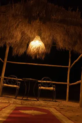 two benches under a straw roof with a table and chairs at Super Luxury camp in Merzouga
