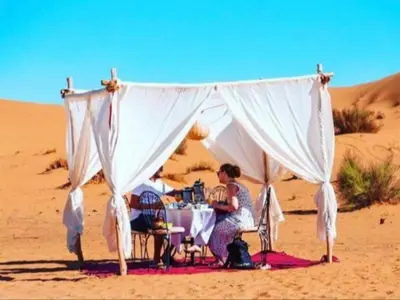 a woman sitting at a table in the desert at Super Luxury camp in Merzouga