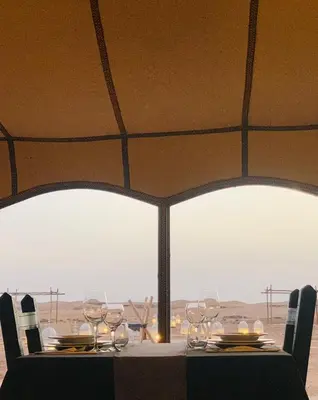 a table with chairs and wine glasses on it at Sahara Dunes Camp in Merzouga
