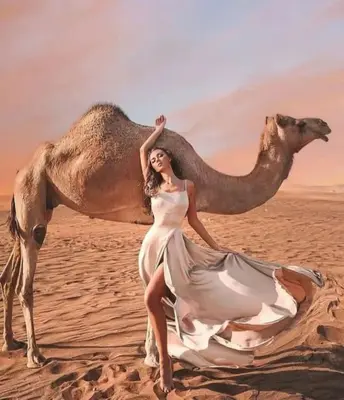 a woman in a dress posing next to a camel at Merzouga Top Luxury Camp in Merzouga