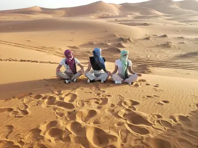 three women sitting on the sand in the desert at Luxury Camp Rachid in Merzouga