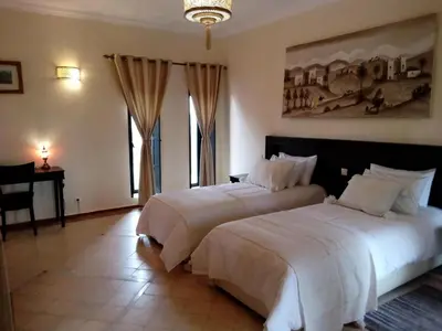 a bedroom with two beds and a desk and windows at Villa Malaa'ika in Marrakech