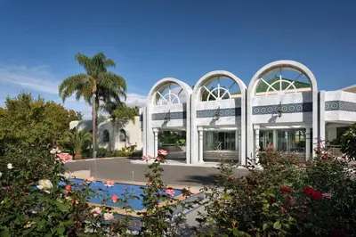 a white building with a palm tree in the background at Fes Marriott Hotel Jnan Palace in Fès