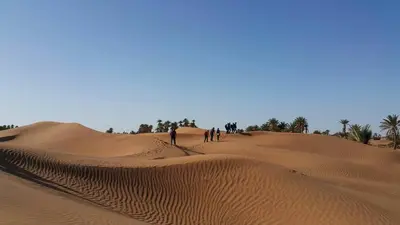 people walking on the sand dunes in the desert at Gîte Assafar in Kalaat MGouna