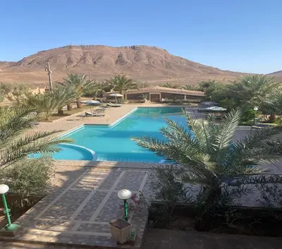 a pool with palm trees and a mountain in the background at La Perle Du Drâa in Zagora