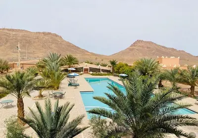 a resort with a pool with palm trees and mountains at La Perle Du Drâa in Zagora