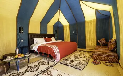 a bedroom with a bed in a tent with a table at Original Luxury Camp in Merzouga