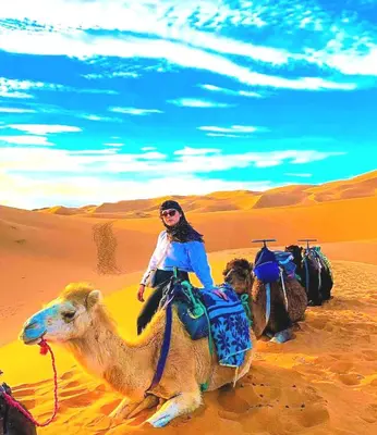 a woman riding a camel in the desert at Original Luxury Camp in Merzouga