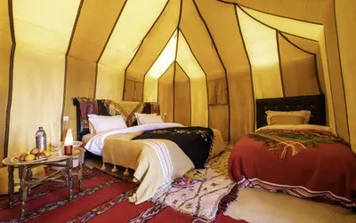 a room with two beds and a table in it at Original Luxury Camp in Merzouga