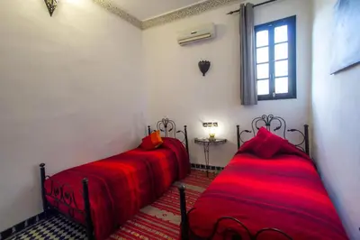 two beds in a room with red sheets and a window at Riad Hala in Fès