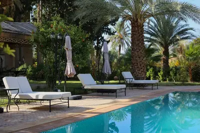 a pool with chairs and umbrellas and palm trees at Kasbah des cyprès in Skoura