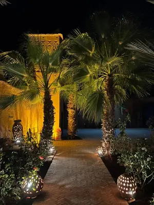 a courtyard with palm trees and lights at night at Kasbah des cyprès in Skoura