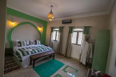 a bedroom with a bed with green walls and windows at Riad Jouba in Merzouga