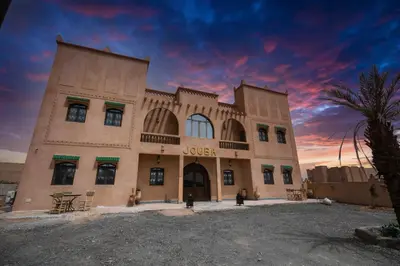 a building with a palm tree in front of it at Riad Jouba in Merzouga