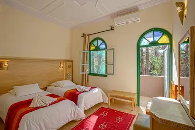 two beds in a room with two windows at Kasbah Sirocco in Zagora