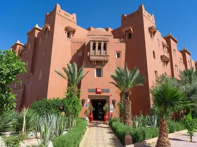 a large brick building with palm trees in front of it at Ibis Ouarzazate Centre in Ouarzazate