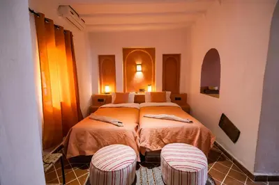 a bedroom with two beds and two stools at Kasbah Mohayut in Merzouga