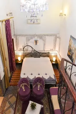 a bedroom with a bed with purple chairs and a chandelier at RIAD YOUSSEF in Fès