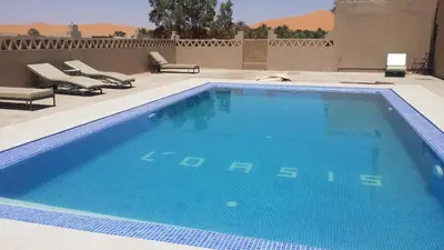 a large blue swimming pool with chairs on a patio at Hotel Riad Oasis in Merzouga