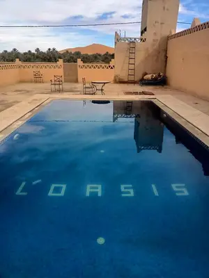 a pool of blue water in front of a building at Hotel Riad Oasis in Merzouga