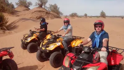 three men are riding atvs in the desert at Le Drom'blanc in Mhamid
