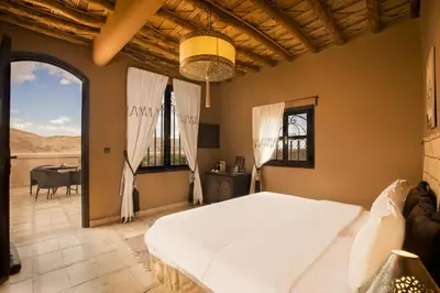 a bedroom with a large white bed and a table at Ksar Ighnda in Aït Ben Haddou
