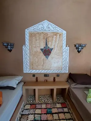 a room with two beds and a table with a painting on the wall at Hotel Riad Sahara Activity in Mhamid