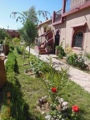 a garden in front of a house with red flowers at La Perle Du Dades in Boumalne