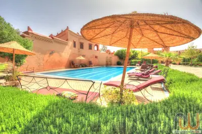 a swimming pool with an umbrella and lounge chairs at La Perle Du Dades in Boumalne