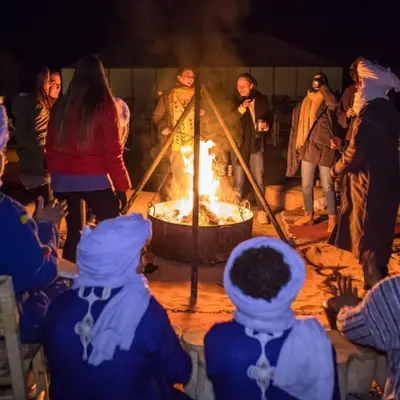 a group of people standing around a large fire at Maktub Desert Luxury Camp in Merzouga
