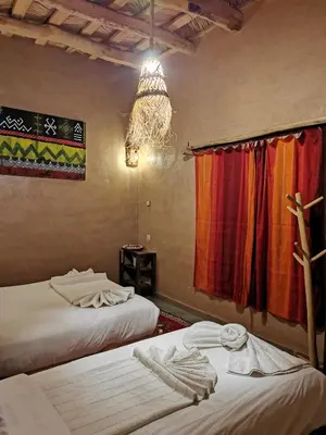 a room with two beds and a window and a chandelier at Maison d'hôte tamatart - Homestay in Kalaat MGouna