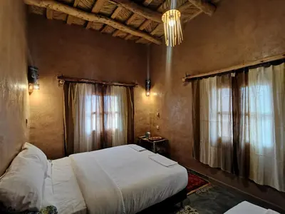 a bedroom with a bed and two windows and a chandelier at Maison d'hôte tamatart - Homestay in Kalaat MGouna