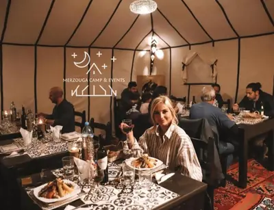 a woman sitting at a table with a plate of food at Merzouga Camp & Events in Merzouga