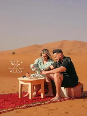 a man and a woman sitting at a table in the desert at Merzouga Camp & Events in Merzouga