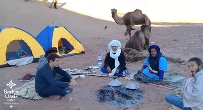 a group of people sitting on the beach with tents at Berber Oasis Camp in Kasr Bounou