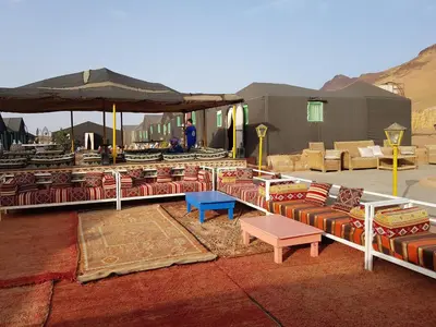 a patio with couches and tables and an umbrella at Desert Camp in Zagora - Camel ride - Easy & Affordable Stays in Zagora