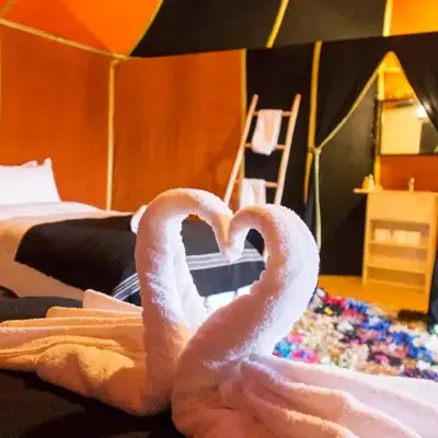 two towel swans making a heart in a bedroom at Horaz Merzouga Camp in Merzouga