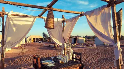 a table in the middle of a desert with white curtains at Horaz Merzouga Camp in Merzouga